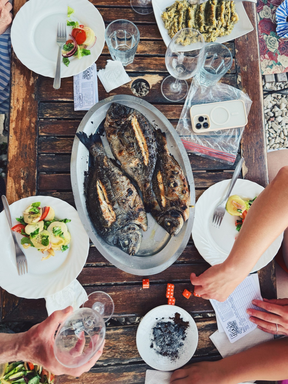 Lunch table from above: grilled fish, salads, and a dice game